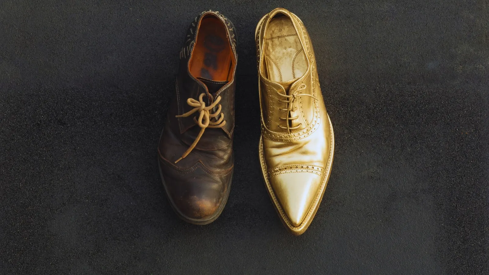 Due scarpe affiancate su un fondo scuro: una di cuoio consumato, una dorata e lucida